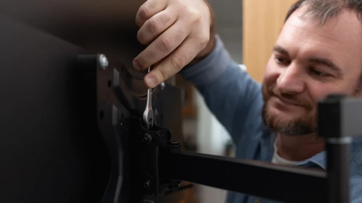 Muž se usmívá a montuje televizi.