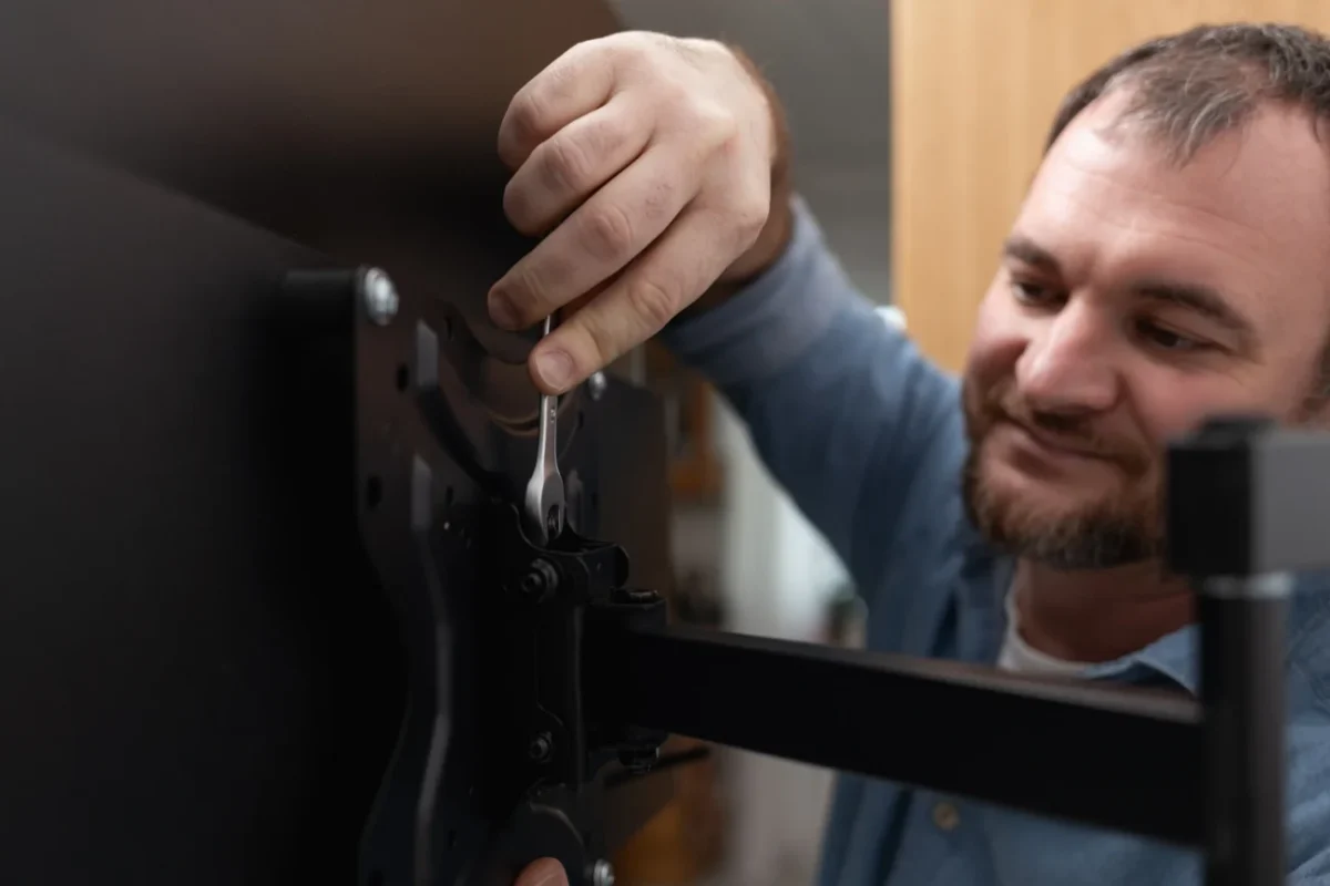 Muž se usmívá a montuje televizi.