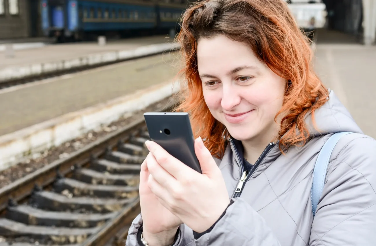 Žena se u kolejí dívá do telefonu.