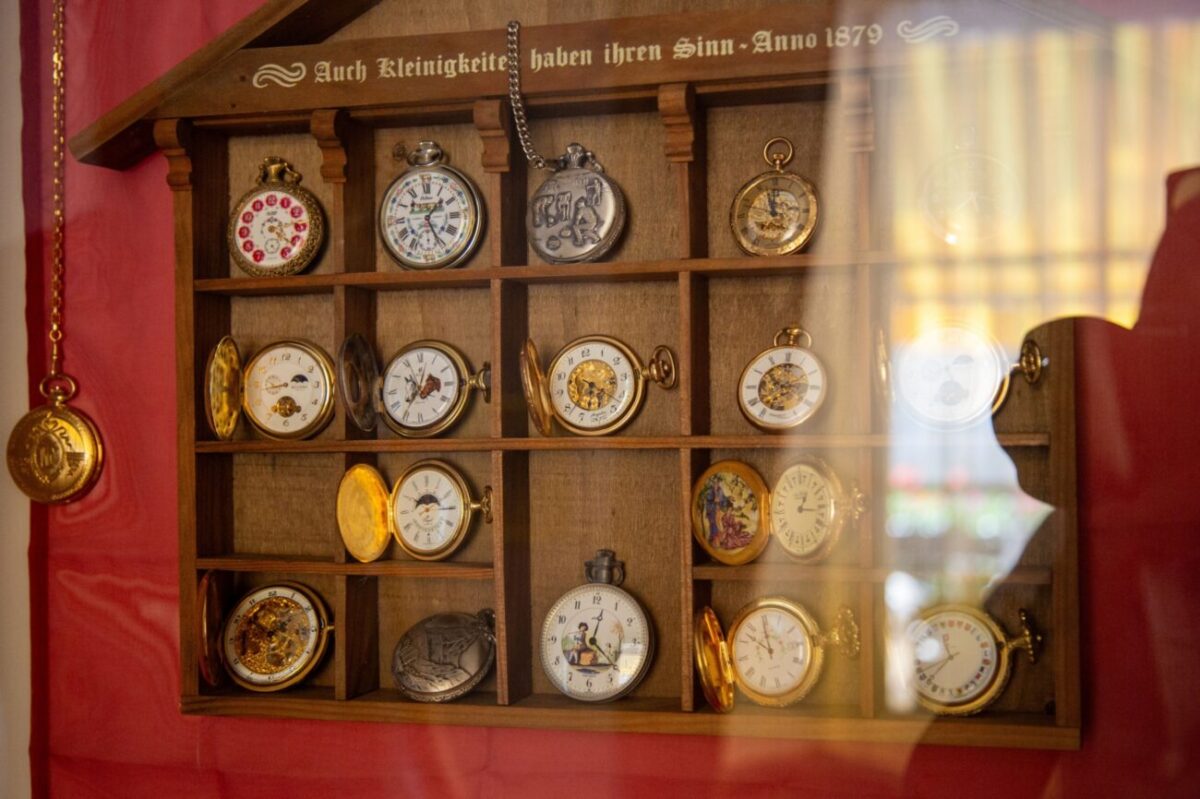 sbírka kapesních hodinek v dřevěné poličce na stěně