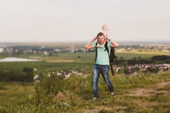 Muž s miminkem se prochází přírodou.