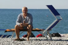 Muž sedící na lehátku na pláži.