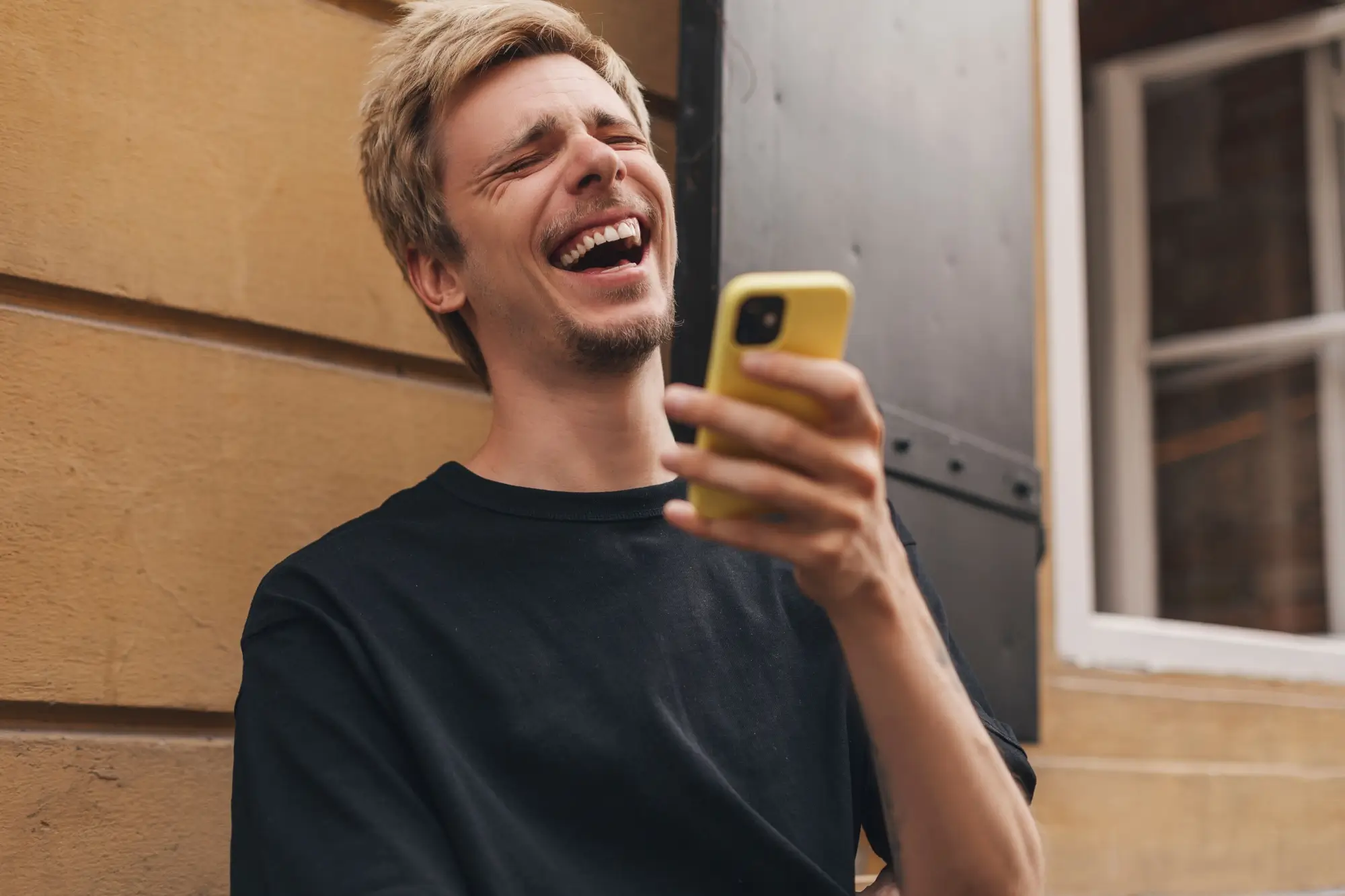 Shutterstock_2153975141 | TVGURU.cz mladý muž se směje čemusi na svém telefonu