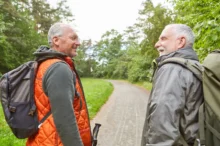 Vitální senioři se na sebe usmívají na procházce lesem s batůžky na zádech