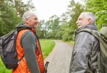Vitální senioři se na sebe usmívají na procházce lesem s batůžky na zádech
