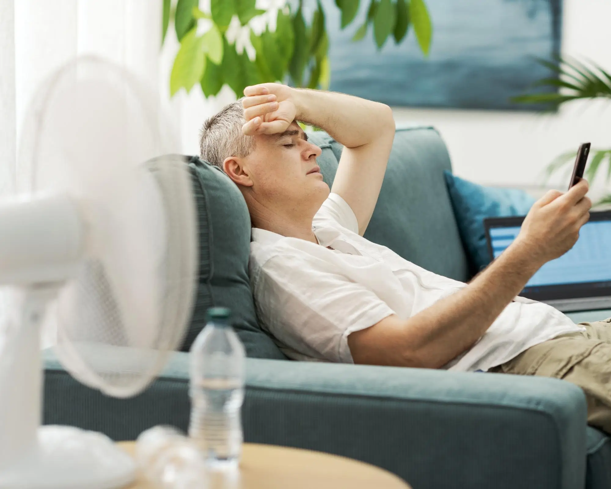 Muž, vyčerpaný horkem, se chladí ventilátorem