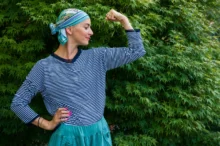 Žena stojí s šátkem na hlavě u keře.