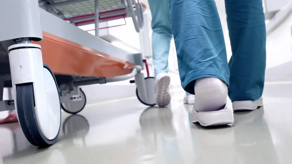 doktoři kráčí vedle pacienta, jdou vidět jen chodidla a kolečka vozíku