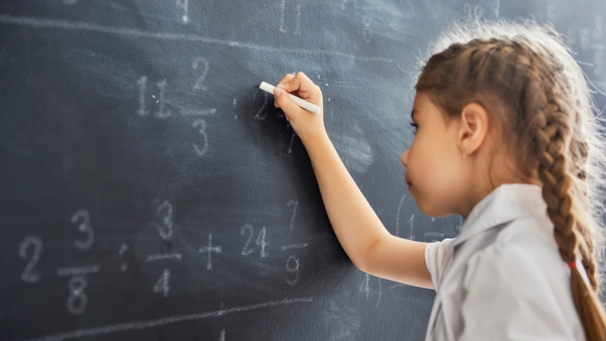 Holčička u tabule řeší matematický příklad.