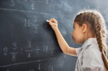 Holčička u tabule řeší matematický příklad.