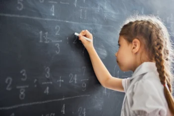 Holčička u tabule řeší matematický příklad.