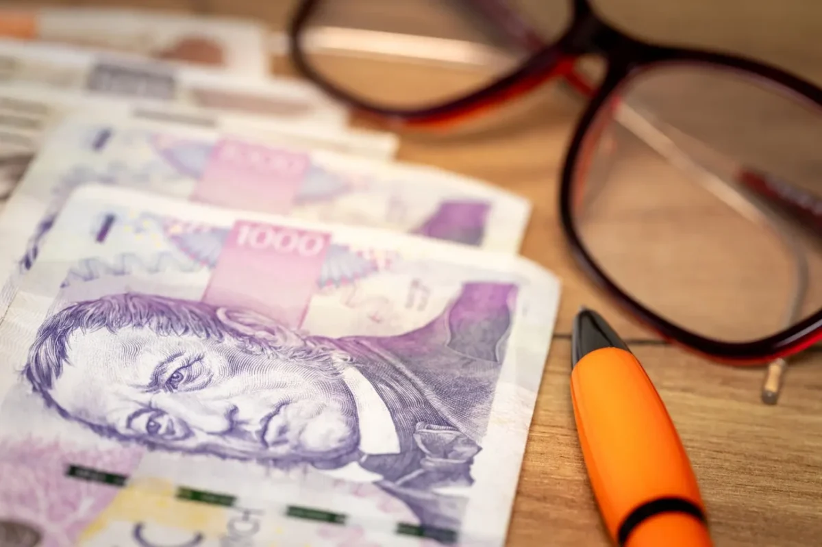 české bankovky na stole vedle brýlí a propisky