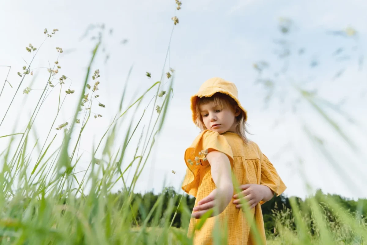 Holčička stojí na louce ve žlutých šatech.