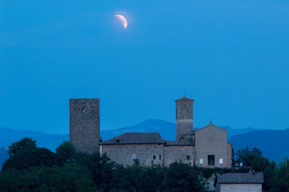 večerní obloha se zatměním měsíce, krajina s malým hradem