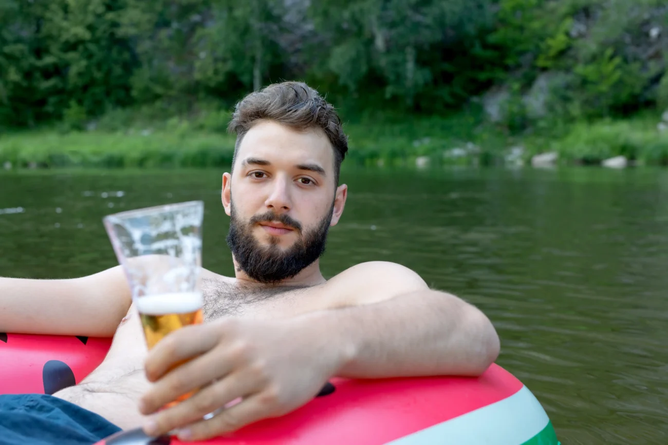 Muž je ve vodě na kruhu a v ruce drží pivo. 
