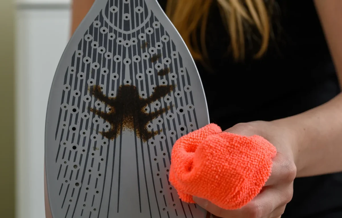 Nečistota na žehličce a žena s hadříkem v ruce.