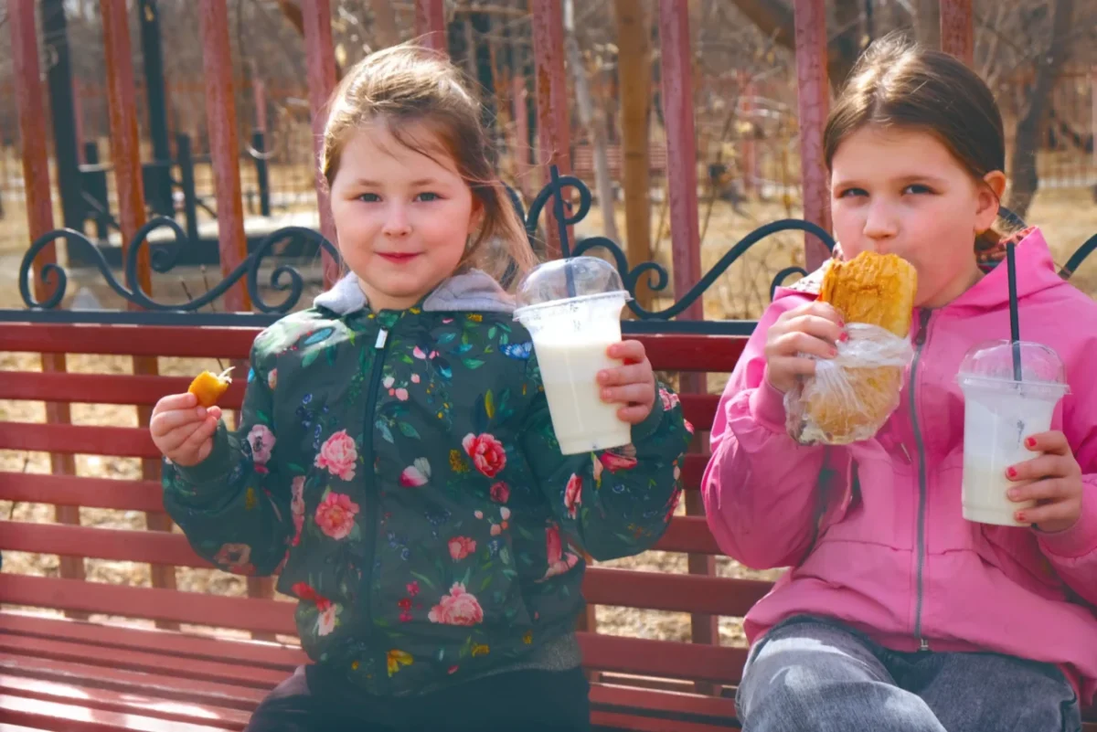 Holčičky sedí venku a mají plné ruce jídla.