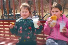 Holčičky sedí venku a mají plné ruce jídla.