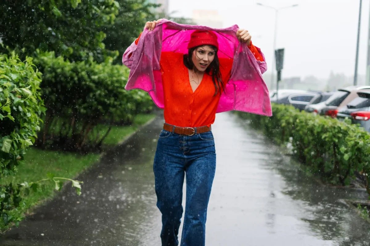 Žena se schovává před deštěm pod bundou.