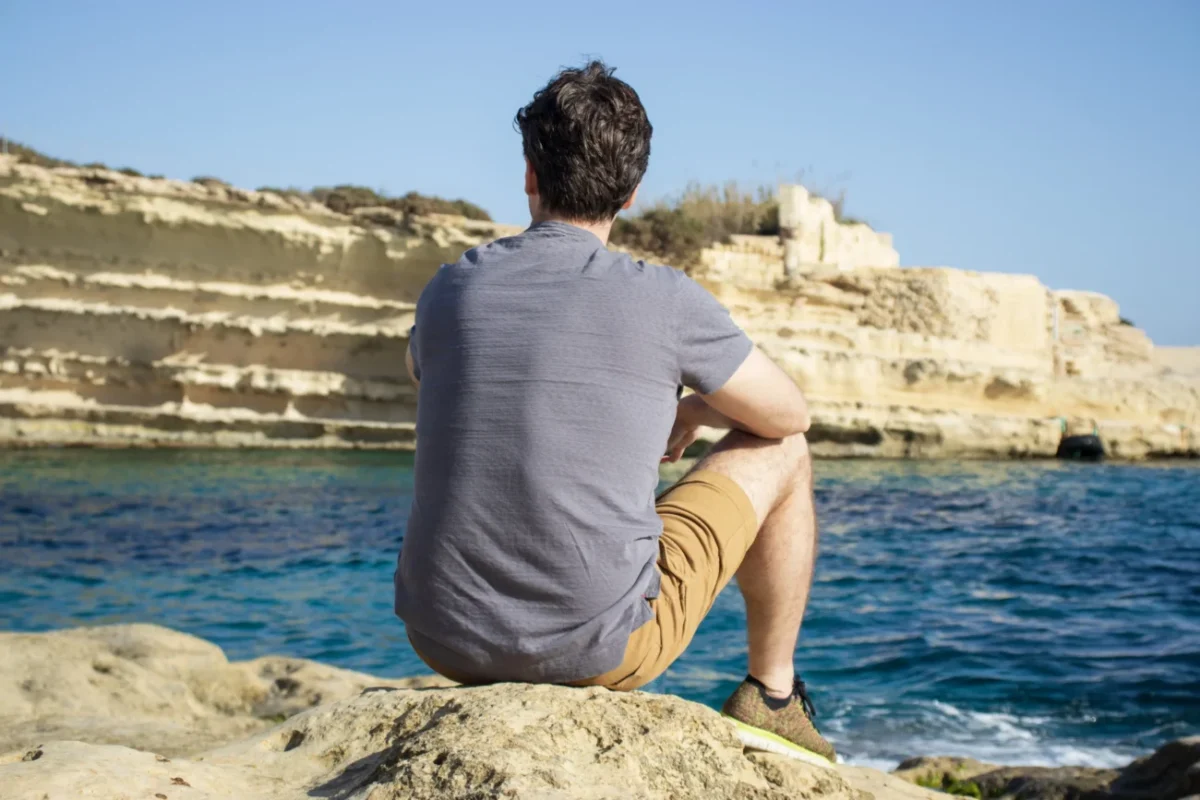 Muž sedí na kameni a dívá se do moře.