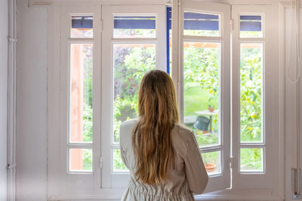 Žena se dívá z okna do zahrady.