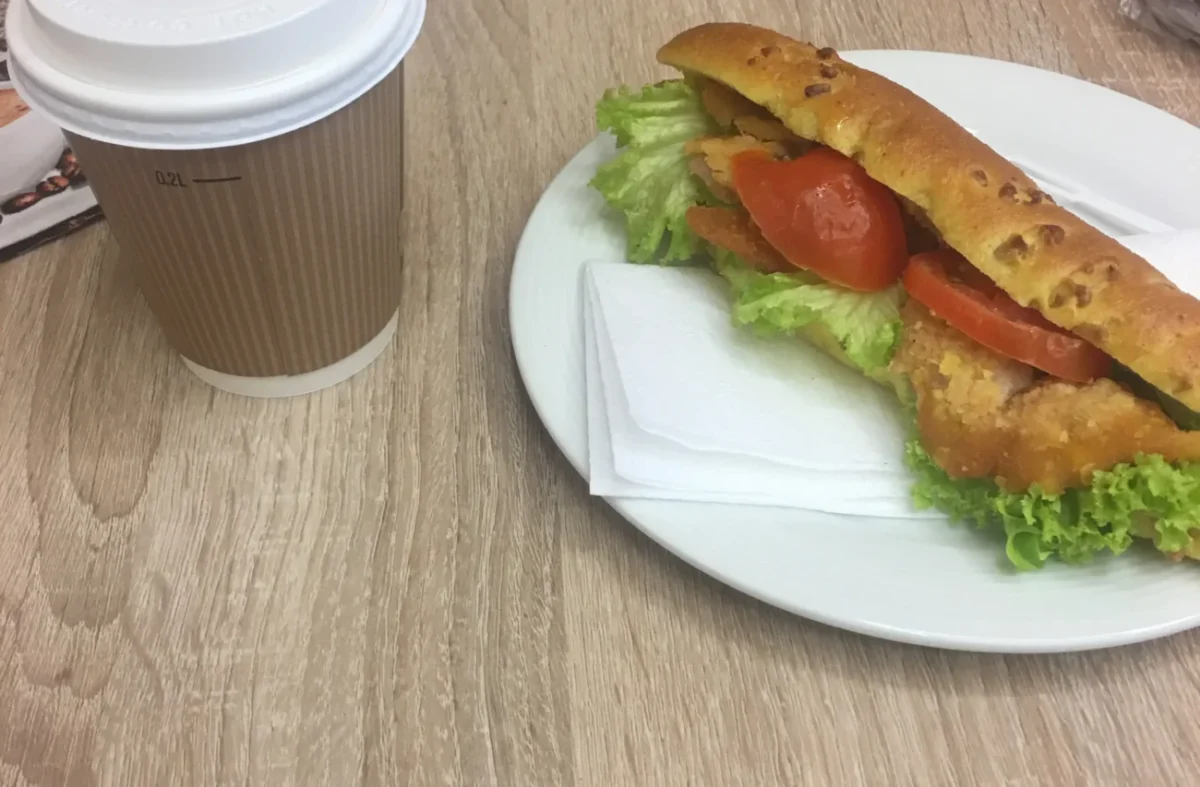 čerstvě připravený sendvič na stole vedle kávy v kelímku