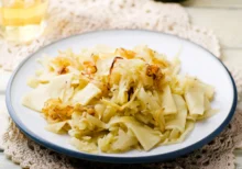 Sedlácká bída - varianta s nudlemi, zelím a sýrem. Mix "kousků" na bílém talíři na stole