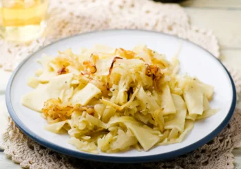 Sedlácká bída - varianta s nudlemi, zelím a sýrem. Mix "kousků" na bílém talíři na stole