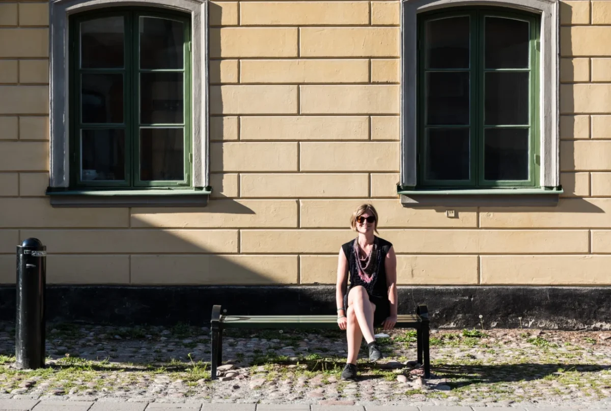 Žena sedí venku na lavičce.