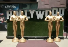 Velké sochy Oscara stojící u nápisu Hollywood.