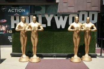 Velké sochy Oscara stojící u nápisu Hollywood.