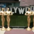 Velké sochy Oscara stojící u nápisu Hollywood.
