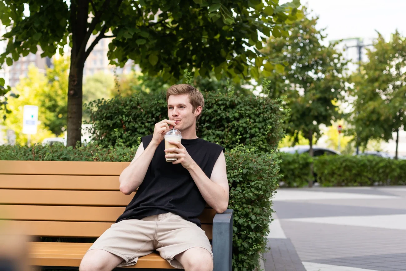 Ledovou kávu si o víkendu moc nevychutnáme. Zdroj: Shutterstock | TVGURU.cz Muž na lavičce, který pije ledovou kávu.