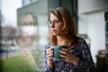 Žena dívající se z okna s hrnkem čaje.