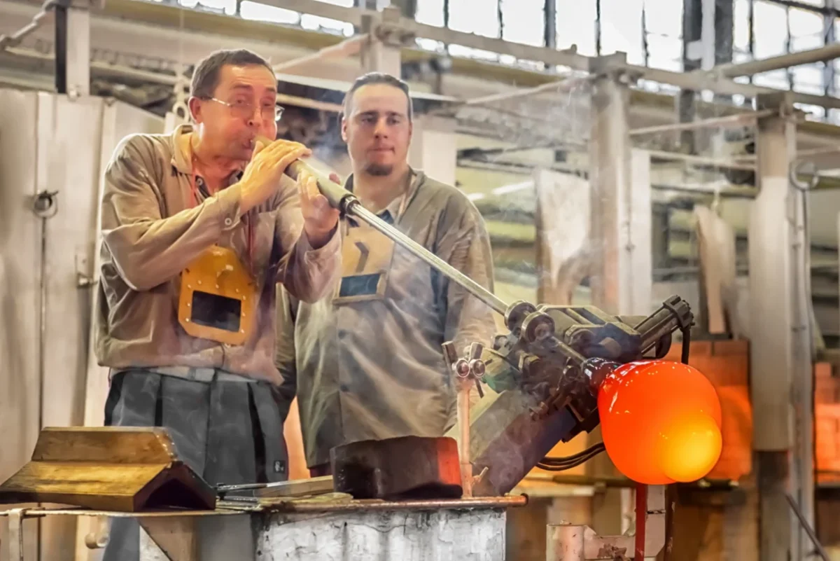 Muži ve sklárně foukají sklo.