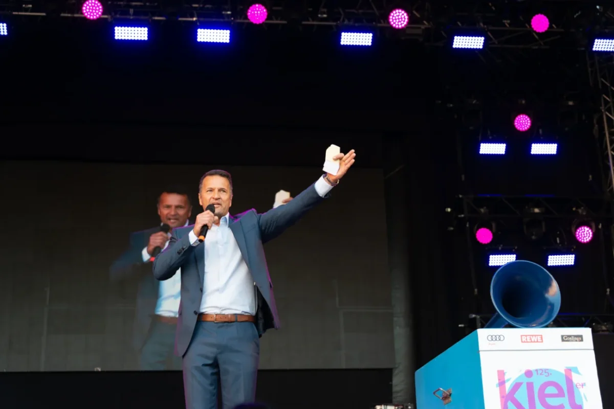 Muž stojí na pódiu s mikrofonem a moderuje.