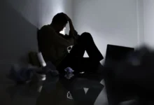 Zdrcený muž sedí na zemi a drží si hlavu.