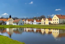 Řada vesnických stavení s rybníkem.