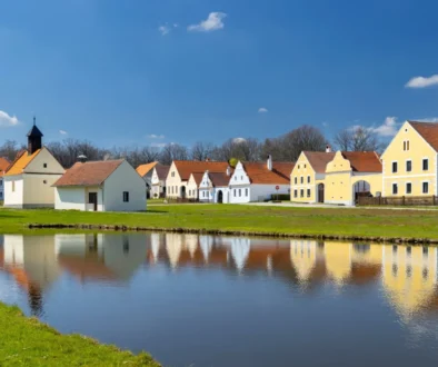 Řada vesnických stavení s rybníkem.