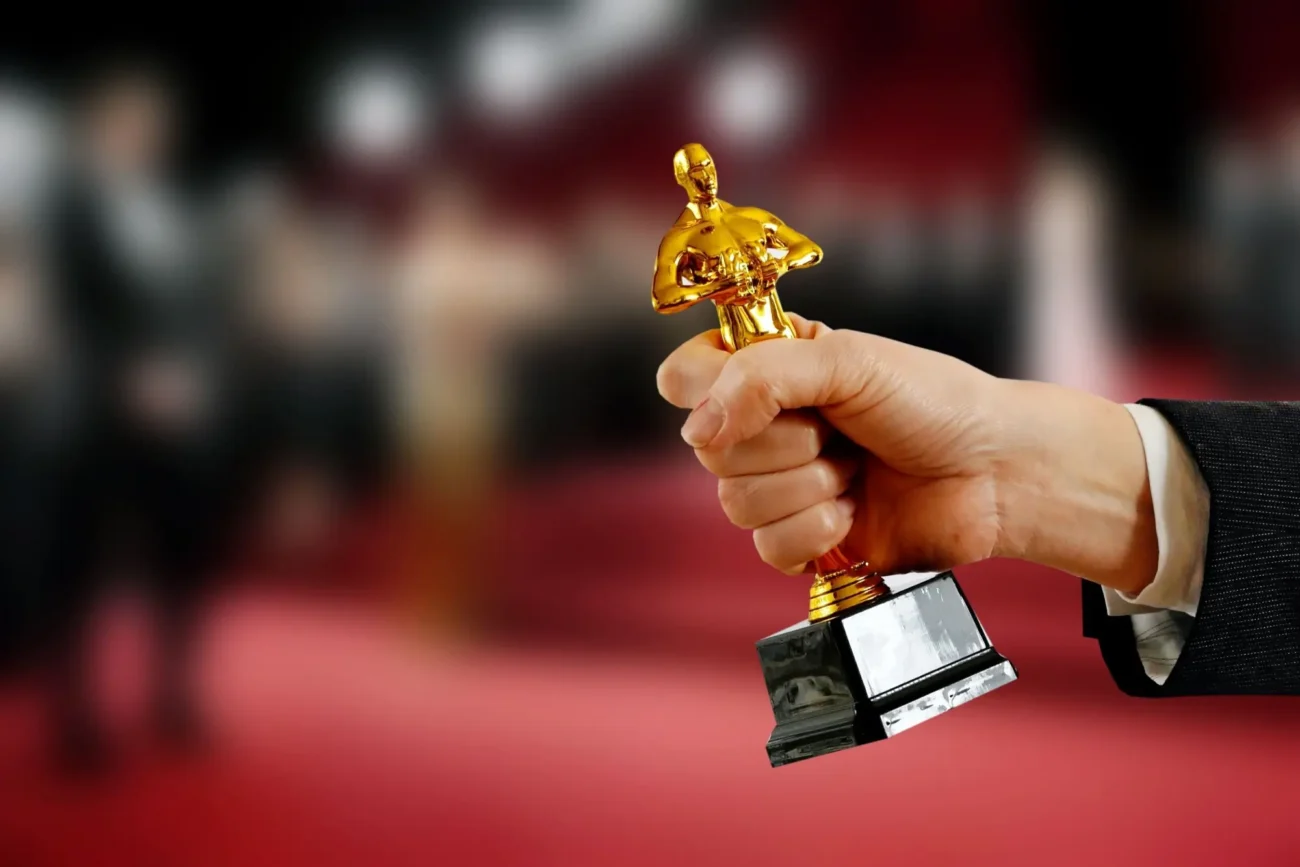 Oscar - zlatá filmová soška | TVGURU.cz Člověk v ruce drží Oscara, zlatou filmovou sošku.