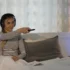 Žena leží v posteli, má sluchátka na uších a míří ovladačem.