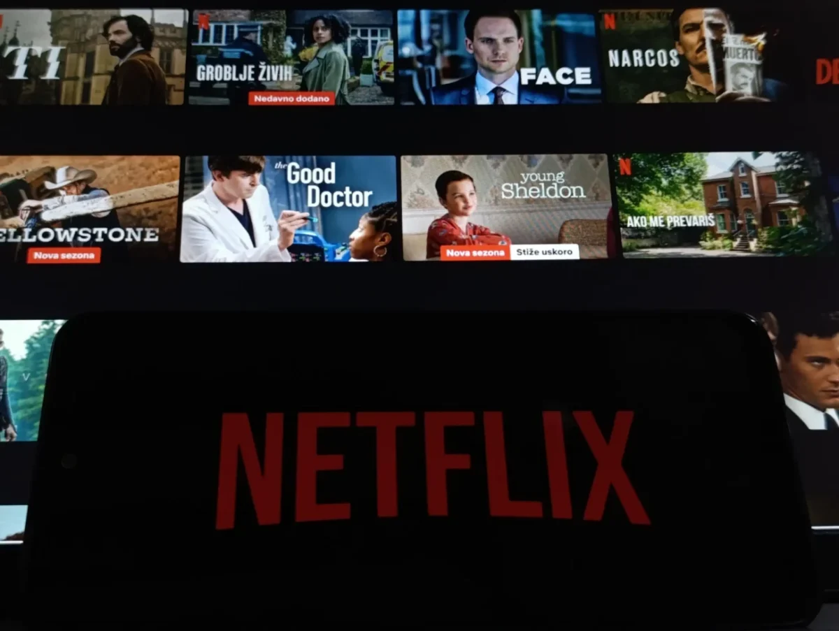 Netflix na telefonu a filmy v pozadí.