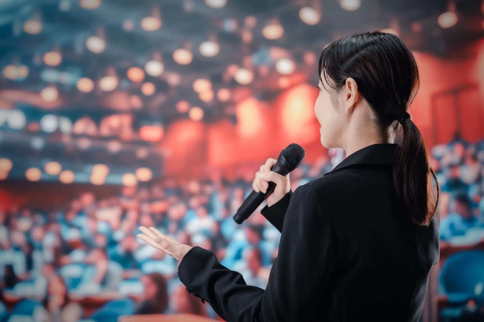 Shutterstock_2438141279 | TVGURU.cz čínská žena mluví do mikrofonu před spoustou lidí