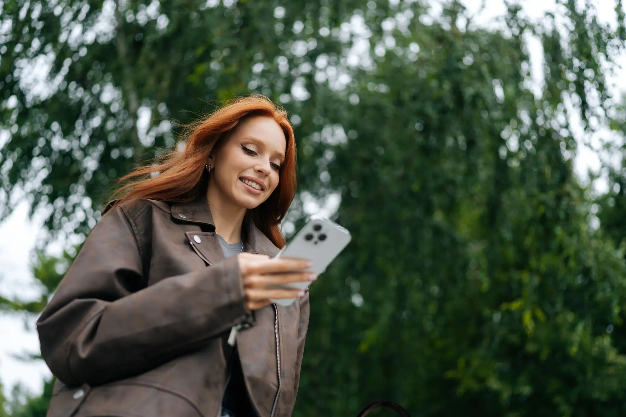 Shutterstock_2511237567 | TVGURU.cz žena kráčí mezi stromy a kouká do telefonu