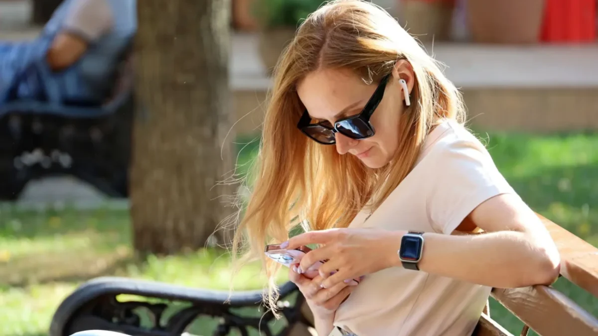 žena sedí na lavičce a dívá se do mobilu