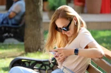 žena sedí na lavičce a dívá se do mobilu