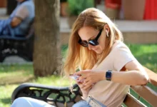 žena sedí na lavičce a dívá se do mobilu
