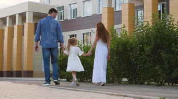 Muž s ženou drží za ruku holčičku a procházejí se venku.