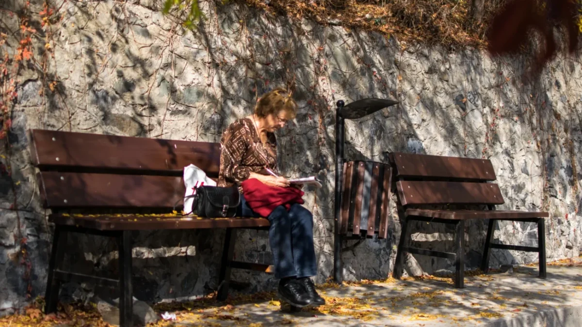 Babička sedí na lavičce a lušti křížovku.
