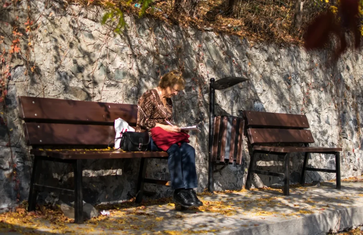 Babička sedí na lavičce a lušti křížovku.